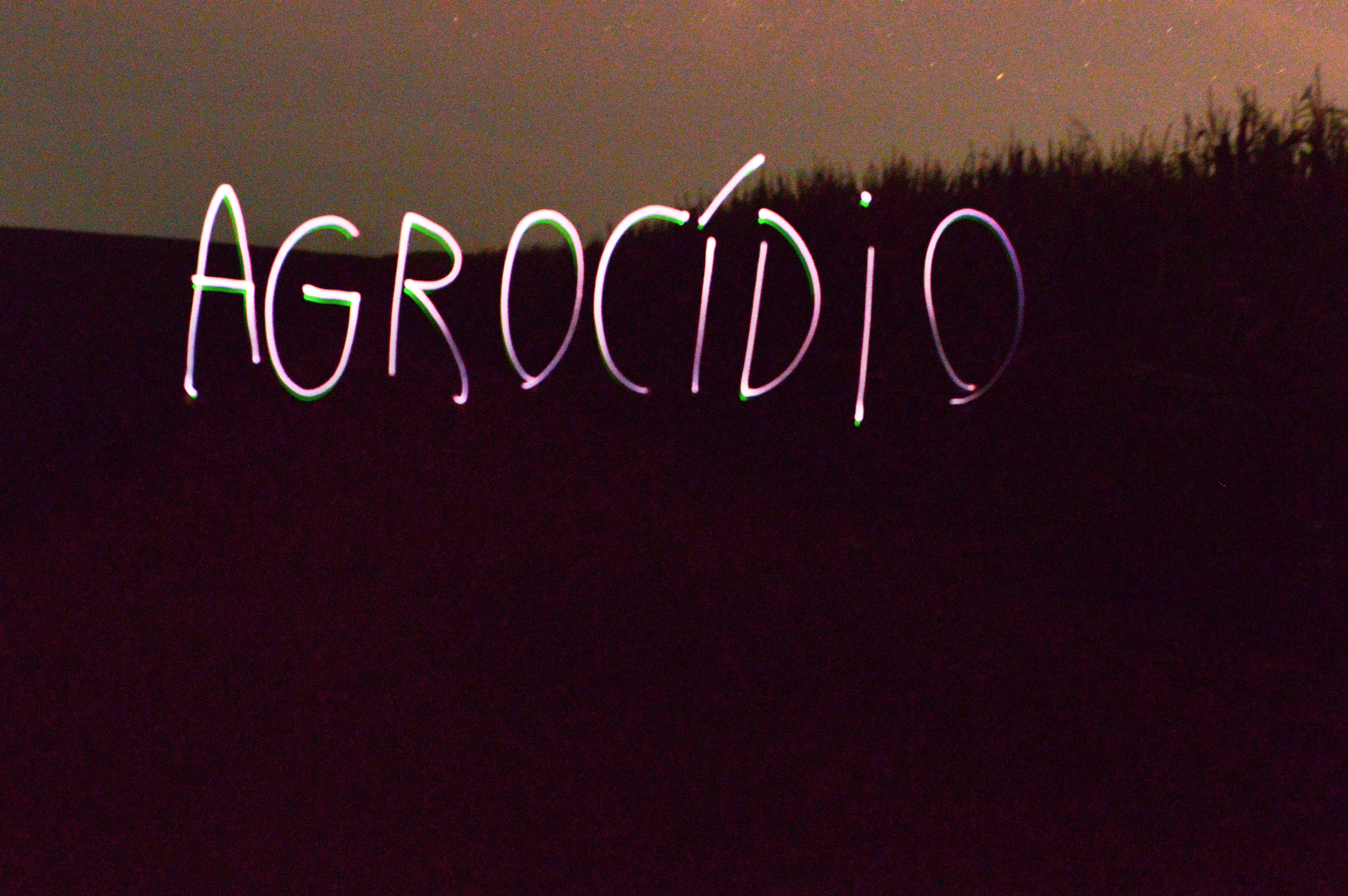 The text 'Agrocidio' written over a dark landscape.
