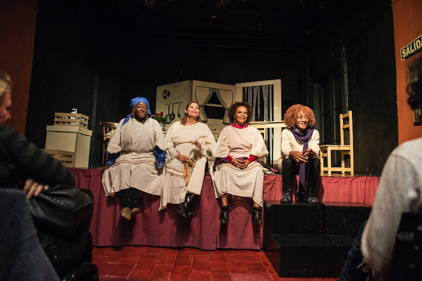 Members of Teatro en Sepia sit on the front of a stage.