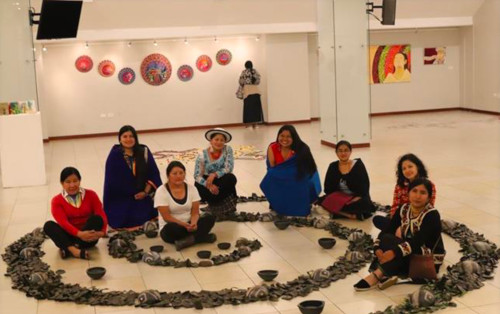 Members of Warmi Muyu pose while sitting amongst an art installation.