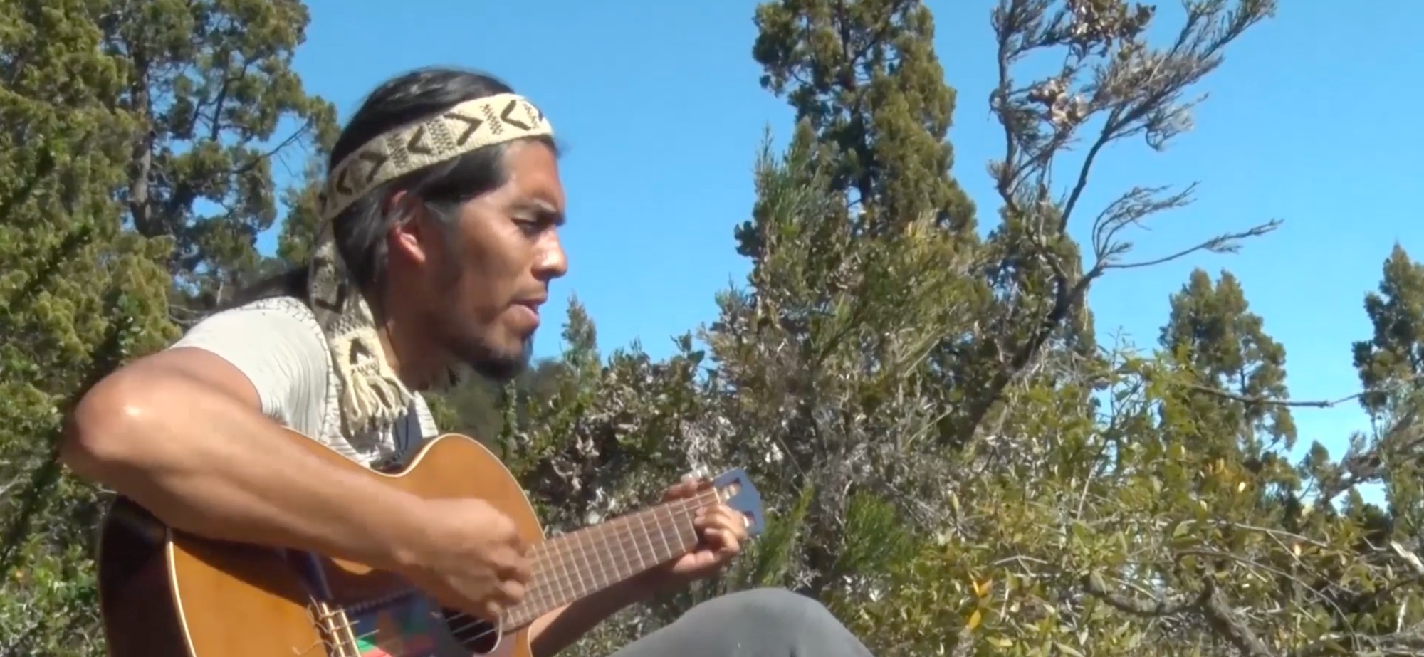 Maxi Flores sits outside, singing and playing his acoustic guitar.