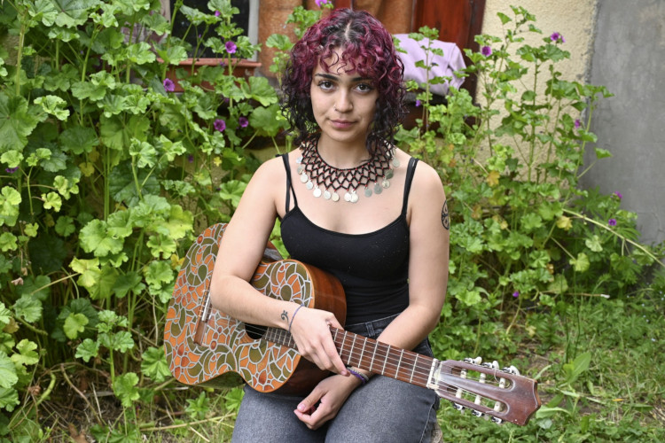 Portrait of Malen Curipan with a guitar in hand in a garden.