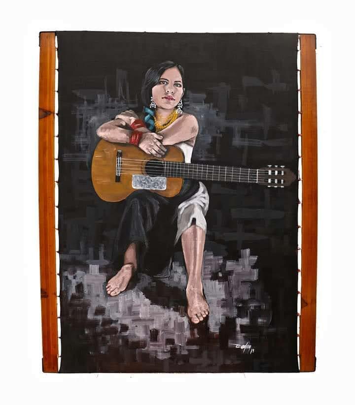 A seated woman rests a guitar across their lap, surrounded by a dark textured background with wooden framing.