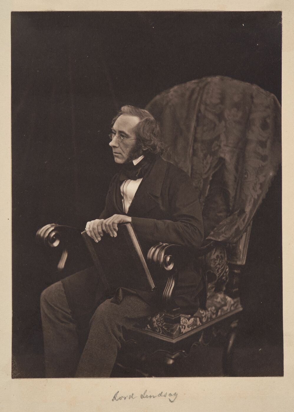 Lindsay is seated in a large chair, leaning forward while holding a book.