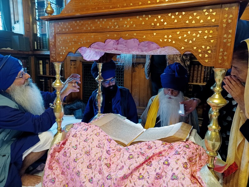 Mahant Giani Tarlochan Singh is seated in front of the Guru, along with three other Nihung Akaali Sikhs. The Guru is placed on its Palki Sahib, with its Rumalla visible too.