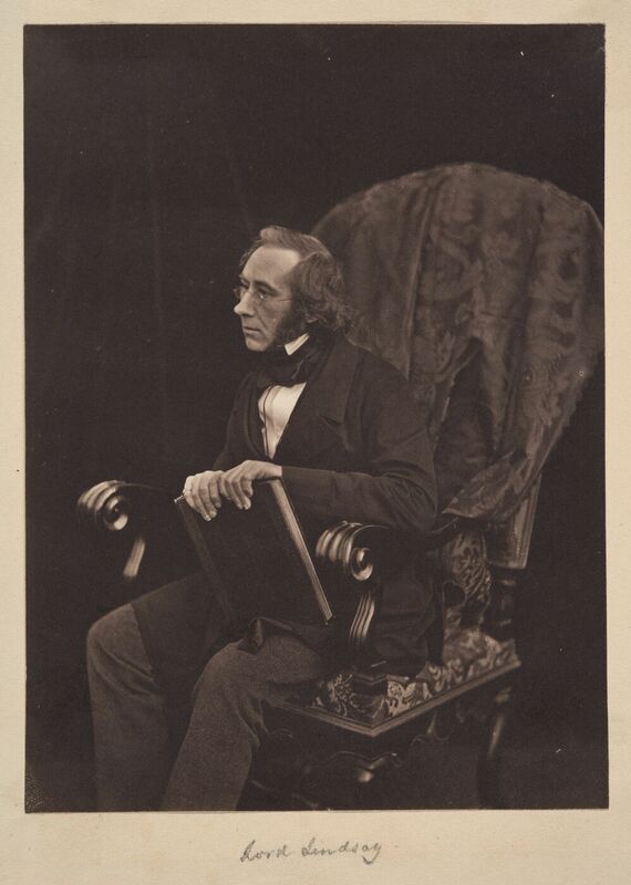 Lindsay is seated in a large chair, leaning forward while holding a book.  