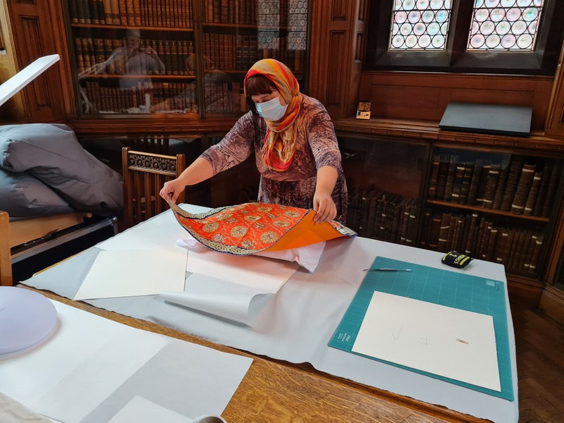 A conservator at Rylands is wearing a head covering while working on conserving the Sri Guru Granth Sahib.